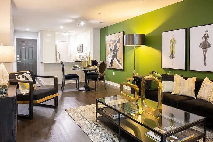 Modern open-concept living room with stylish decor, green accent wall, and cozy seating next to a sleek kitchen area.