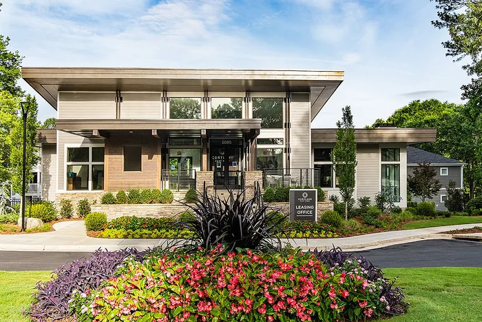 Modern leasing office with sleek architecture, surrounded by vibrant landscaped gardens and lush greenery.