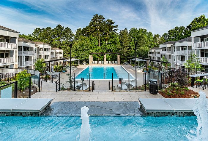 Luxurious apartment complex with a stunning outdoor pool area, surrounded by lush greenery and elegant balconies for a serene living experience.