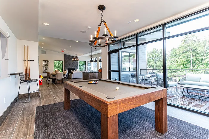 Luxurious apartment lounge featuring a modern pool table, elegant seating, and floor-to-ceiling windows with lush views.
