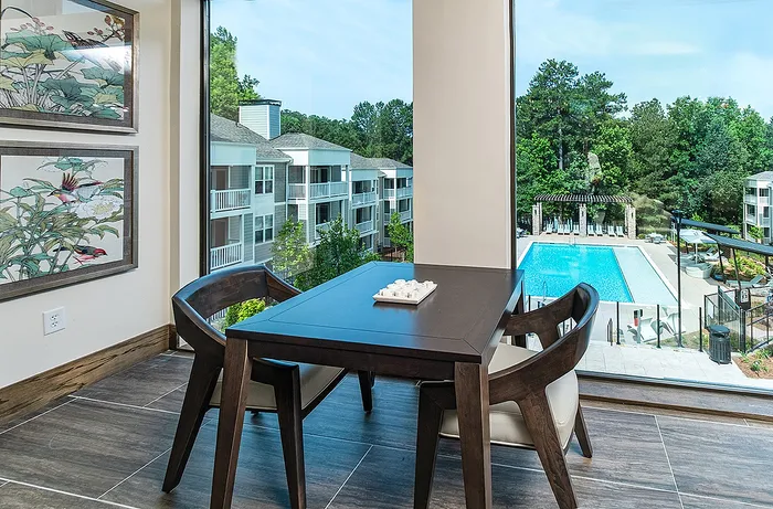 Chic dining area with modern furniture overlooking a stunning pool and lush greenery through expansive windows.
