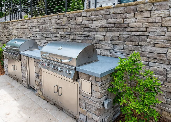 Elegant outdoor kitchen with dual stainless steel grills and stone backsplash, perfect for sophisticated entertaining.