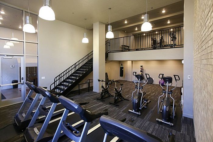 Modern gym with cardio equipment, an upper-level workout area, and sleek design elements.