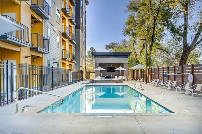 Elegant apartment complex featuring a serene outdoor pool with modern lounge chairs and lush landscaping for ultimate relaxation.