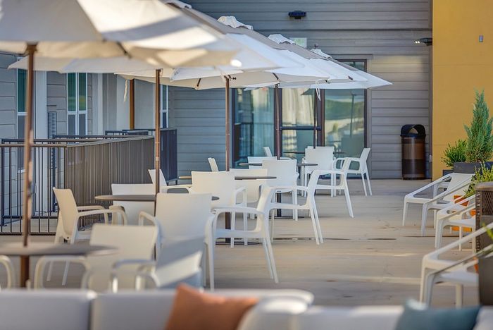 Chic, sunlit patio with elegant white seating and stylish umbrellas, offering a perfect space for relaxation and social gatherings.