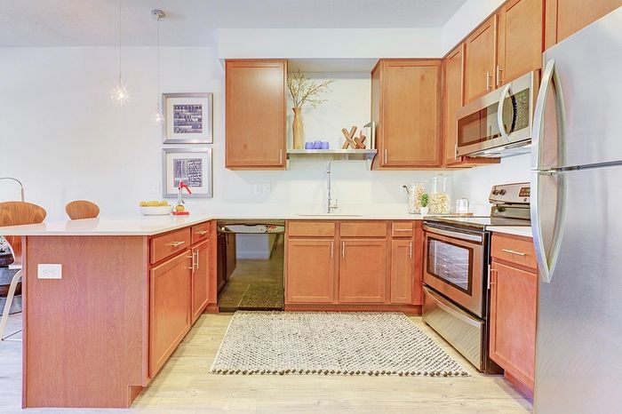 Apartments in Millcreek UT with In-Unit Washer and Dryer - VIA - Modern Kitchen with Warm Wood Cabinetry, Stainless Steel Appliances, and Pendant Lighting