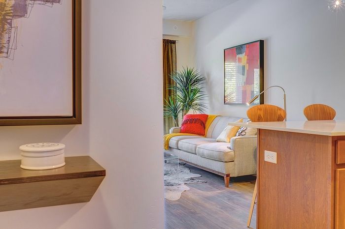Charming apartment interior with a cozy sofa adorned with colorful pillows, modern artwork, and a sleek kitchen island creating an inviting living space.