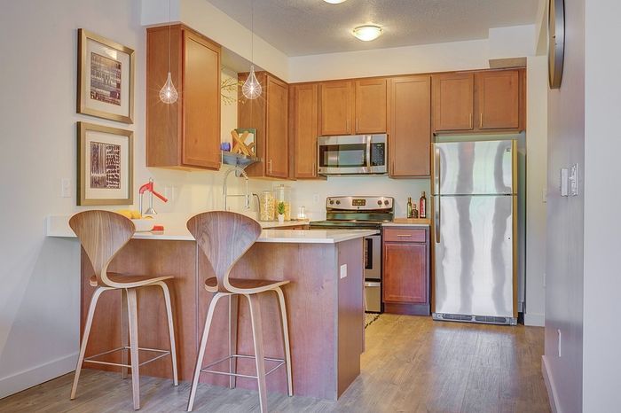 One Bedroom Apartments in Millcreek UT - ViA - Modern Kitchen with Stainless Steel Appliances, Pendant Lighting, Wood-Style Flooring, and Marble Countertops.
