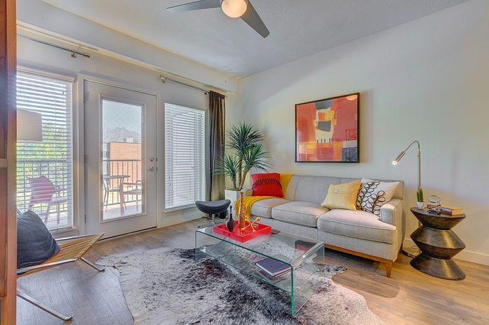 1 Bedroom Apartments in Millcreek UT - ViA - Spacious Living Room with Large Windows, Wood-Style Flooring, Tall Ceilings with Ceiling Fan, and a Windowed Door Leading to a Private Balcony.