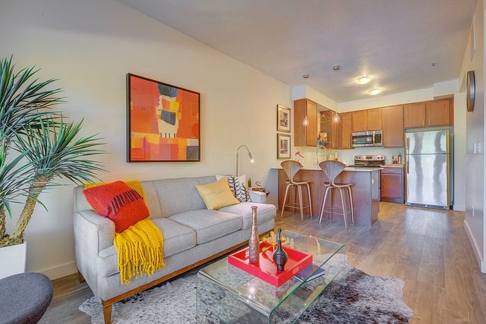 Inviting open-concept living area with stylish decor featuring a cozy gray sofa, vibrant art, and sleek kitchen with modern appliances. Ideal for entertaining.