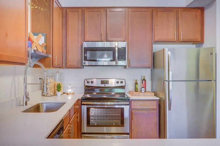 Quiet Apartments in Salt Lake City, UT - ViA - Kitchen With Warm Wood Cabinets, White Countertops, Stainless Steel Appliances, and Deep Sink With Pull-Down Faucet.