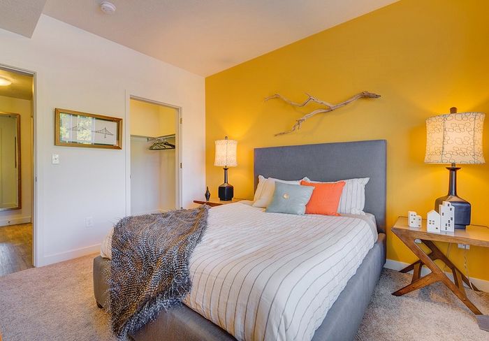 Pet-Friendly Apartments in Salt Lake City, UT - ViA - Cozy Bedroom With Yellow Accent Wall, Upholstered Bed, Layered Pillows, Soft Carpet, and Nightstands With Warm Table Lamps