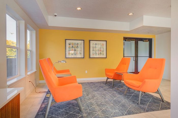 Modern sitting area with vibrant orange chairs, elegant geometric artwork, and a cozy atmosphere highlighted by a sunny yellow accent wall.