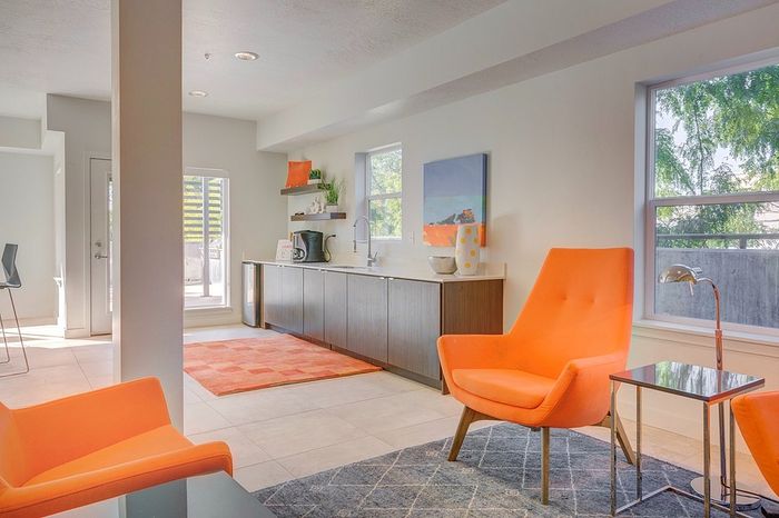 Bright and modern living space with vibrant orange chairs, sleek cabinetry, and abundant natural light.