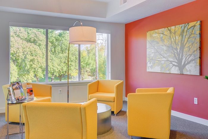 Bright and inviting living room with vibrant yellow chairs, modern floor lamp, and large window offering lush views.