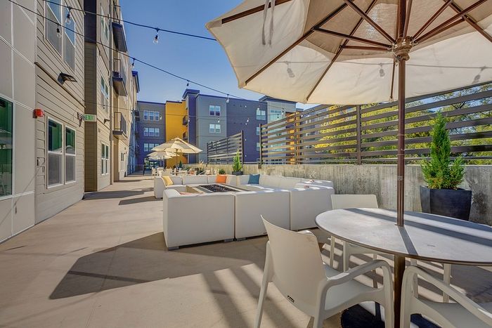 Chic outdoor lounge area featuring modern white seating, vibrant pillows, and large umbrellas under a clear blue sky, perfect for relaxation and social gatherings.
