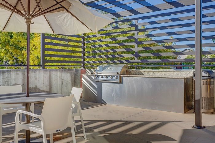 2 Bedroom Apartments in Millcreek UT - VIA - Outdoor Grill with seating and picnic tables, surrounded by modern fence and greenery