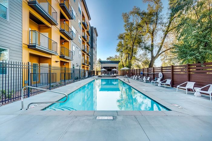 Millcreek UT Studios for Rent - ViA - Sparkling Swimming Pool, Surrounded by Lounge Seating, Umbrellas, a Large Cabana with TV, and Spa.