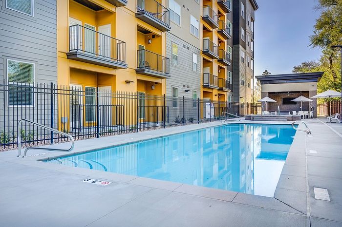 Modern apartment complex with inviting outdoor pool, surrounded by stylish balconies and sun loungers for a relaxing lifestyle.