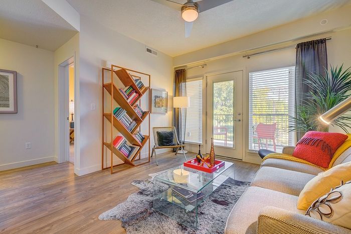 Modern living room with elegant decor, featuring a stylish glass coffee table, cozy sofa, and a unique geometric bookshelf. Abundant natural light floods through large windows leading to a balcony.