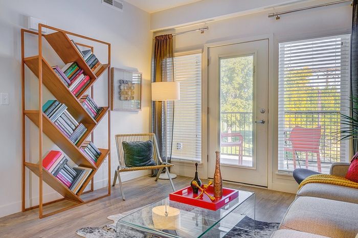 Chic living room with modern geometric bookshelf, cozy seating, and bright natural light from large windows overlooking a serene balcony.