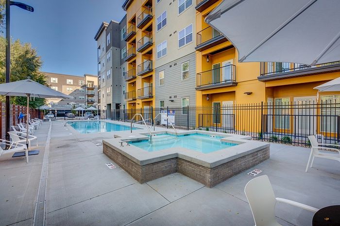 Modern apartment complex with vibrant exterior featuring a luxurious swimming pool and spa, surrounded by chic lounge chairs and spacious umbrellas.