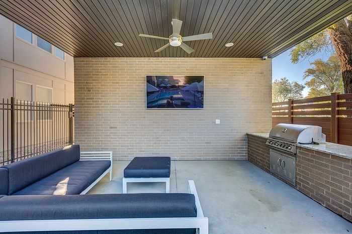 Modern outdoor patio with sleek seating, a wall-mounted TV, and built-in barbecue grill, perfect for entertaining.