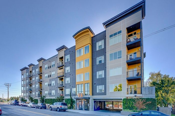 Modern apartment building with vibrant exterior, featuring balconies and lush greenery at the entrance.