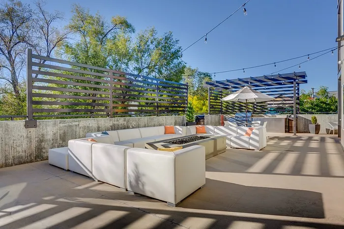 Luxurious outdoor patio with stylish white seating, modern fire pit, and elegant string lighting against a backdrop of lush greenery.