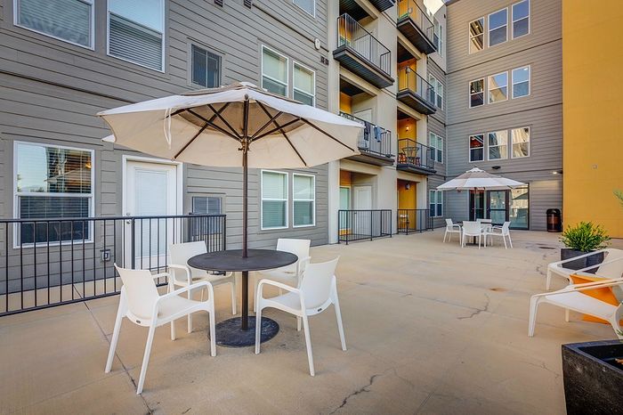 Charming outdoor patio area with stylish seating, large umbrellas, and modern apartment architecture.