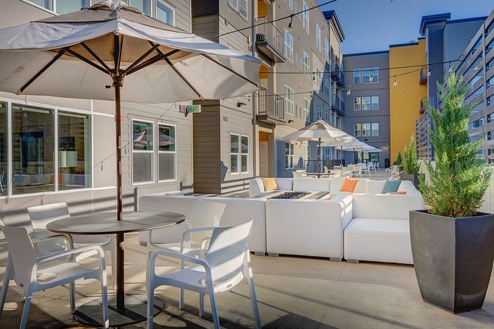 Chic apartment courtyard featuring modern patio furniture, large umbrellas, and lush greenery for a relaxing outdoor lounge experience.