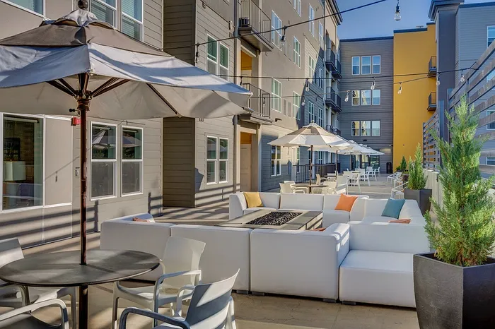 Chic outdoor patio with modern seating, vibrant cushions, and large parasols, perfect for relaxation and social gatherings in an upscale apartment complex.