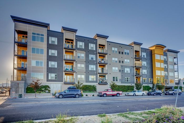 Modern apartment building with sleek design, large windows, and balconies set against a clear sky.