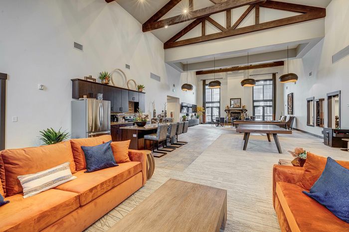 Luxurious open-concept loft with high wooden beam ceilings, modern kitchen, and stylish seating area featuring vibrant orange couches.