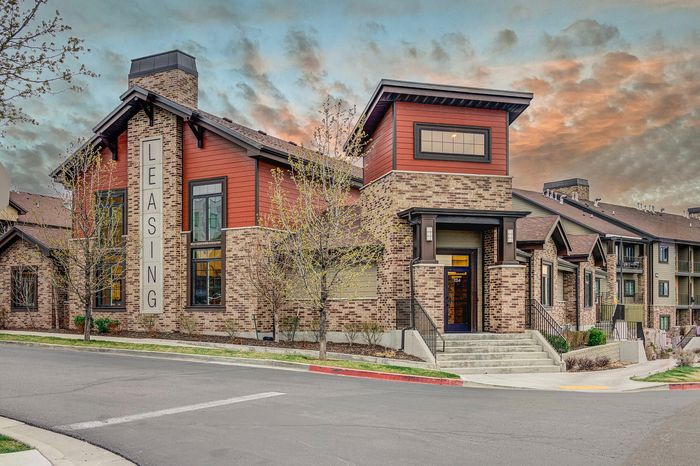 Modern leasing office building with stylish brick and red siding, set against a dramatic sunset sky.