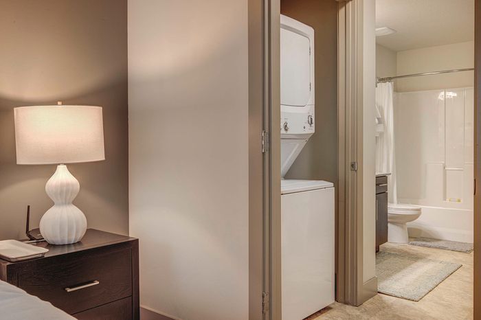 Cozy apartment corner with sleek in-unit washer and dryer, a stylish bedside lamp, and modern bathroom access.