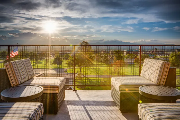 Stunning apartment balcony with comfortable seating, offering a breathtaking view of lush greenery and a vibrant sunset.