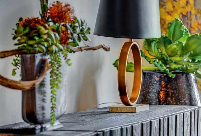 Elegant interior decor featuring a modern table lamp with a gold ring design, complemented by lush green plants and vibrant floral arrangements.