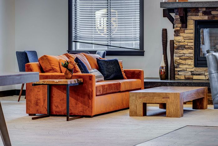 Inviting living room showcasing a plush orange sofa adorned with blue cushions, complemented by a rustic stone fireplace and modern wooden coffee table, exuding warmth and style.