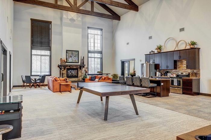 Luxurious open-concept living area featuring high ceilings, a modern kitchen, and a cozy fireplace with elegant seating and a unique ping pong table.