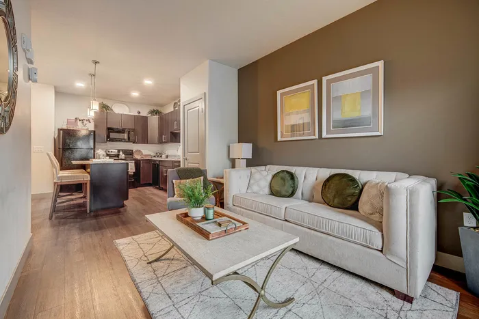 Modern open-concept living area with elegant decor, featuring a cozy sofa, stylish coffee table, and a sleek kitchen with dark cabinetry.