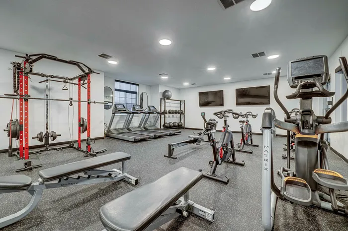 Modern fitness center with state-of-the-art equipment including treadmills, exercise bikes, and weightlifting stations in a spacious, well-lit room.