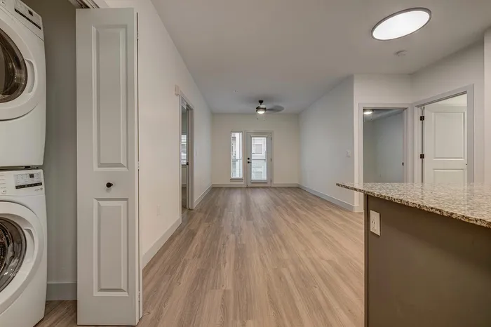 Bright and spacious apartment interior featuring modern laminate flooring, a built-in washer and dryer, and large windows with abundant natural light.