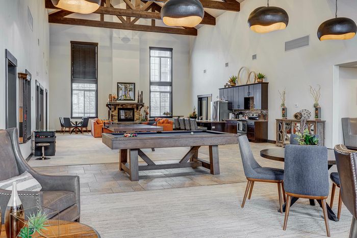 Elegant communal lounge with vaulted ceilings, featuring a stylish pool table, modern kitchen, and cozy seating around a grand fireplace.