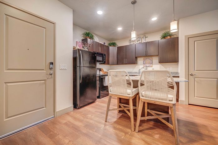 Modern kitchen with sleek dark cabinets, granite countertops, and stylish wicker chairs, illuminated by elegant pendant lighting.