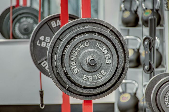 Close-up of gym weight plates stacked on a barbell with sleek kettlebells in the background, capturing a modern fitness space.