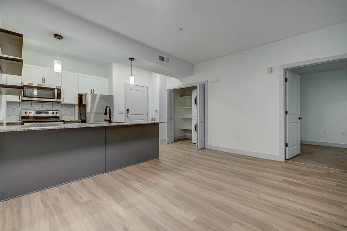 Sleek modern kitchen with granite countertops, stainless steel appliances, and elegant lighting, adjacent to a spacious open living area featuring wood flooring.