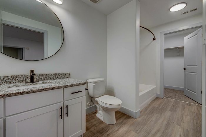 Modern bathroom with elegant granite countertop, oval mirror, and wood-style flooring showcasing luxury design.