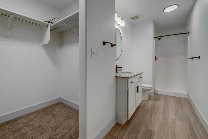 Modern bathroom with elegant vanity, round mirror, and walk-in closet, boasting sleek finishes and a spacious design.