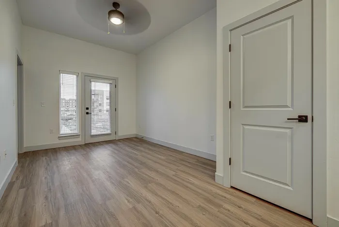 Bright and modern empty room with sleek wooden flooring, large windows, and a stylish ceiling fan, perfect for personalization and comfort.